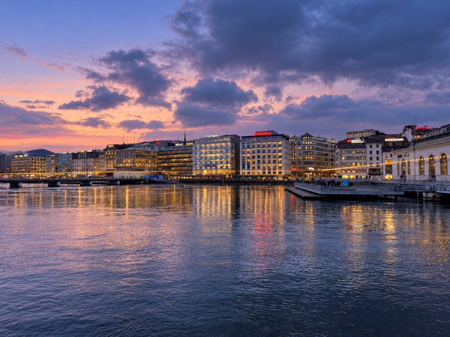 Enseignes lumineuses en toiture se reflétant dans le Rhône au coucher du soleil, Genève